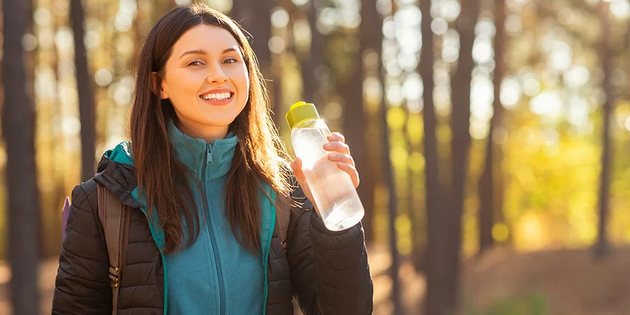 Smiling young woman drinking water while hiking. cbd for women's wellness. Buy CBD for women's issues.